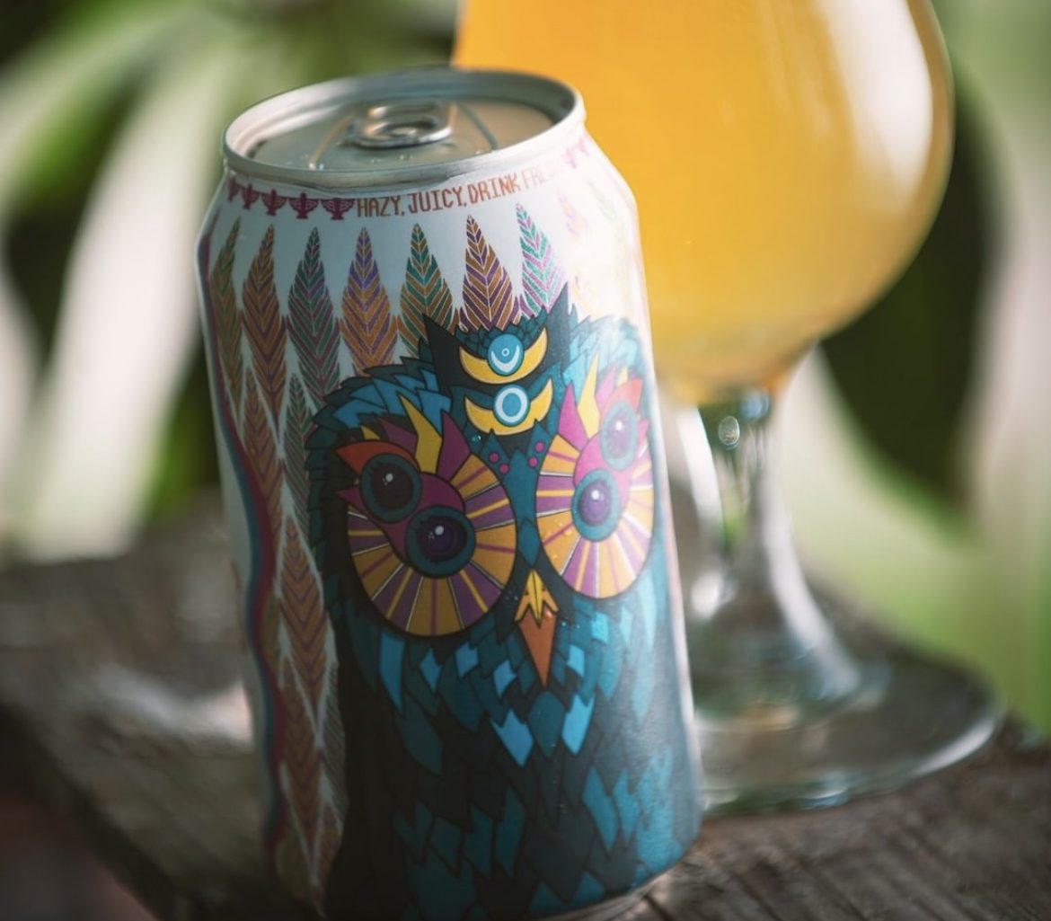 A full-body shrink sleeve with wrap-around artwork on a beer can, next to a poured glass.